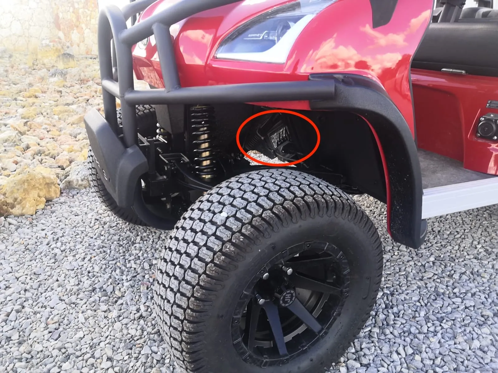 Parte delantera de un carrito de golf rojo, con la toma de carga detrás de la rueda delantera marcada